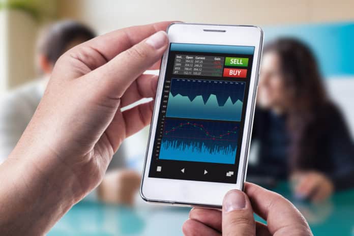 A woman holding a smart phone running a trading or forex app with charts and data. Dario Lo Presti / Shutterstock.,com